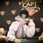 Ein Mann und eine Frau sitzen an einem Pokertisch und spielen Karten. Der Mann hat eine Hand voll Karten, während die Frau nachdenklich auf ihre Karten schaut. Im Hintergrund sind Pokerchips und Get