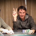 Ein Mann und eine Frau sitzen an einem Pokertisch und spielen Texas Hold'em. Der Mann hat eine große Hand mit Pokerchips vor sich, während die Frau nachdenklich ihre Karten betrachtet. Die Szene spielt