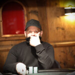 Ein Mann spielt Poker an einem eleganten Tisch in einem stilvollen Casino, umgeben von anderen Spielern und einer glamourösen Atmosphäre.