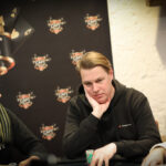 Ein Paar Männer spielen Poker an einem eleganten Tisch in einem luxuriösen Casino. Die Männer sind konzentriert und haben Stapel von Chips vor sich liegen. Die Szene strahlt eine Atmosphäre von Span