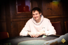Ein Mann, der an einem Pokertisch sitzt, Karten hält und konzentriert auf seine Hand schaut, umgeben von anderen Spielern in einem Casino.