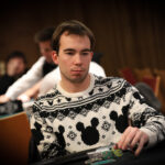 Ein Mann und eine Frau spielen Poker an einem eleganten Tisch, umgeben von goldenen Pokerchips und Karten. Der Mann hat eine Hand am Kinn und schaut nachdenklich, während die Frau konzentriert ihre