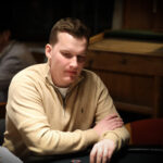 Ein Mann und eine Frau sitzen an einem Pokertisch und spielen eine Partie Poker. Der Mann hat eine Hand mit Karten vor sich liegen, während die Frau ihre Karten noch hält. Im Hintergrund sind Pokerchips
