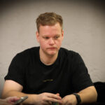 Ein buntes Pokertisch-Layout mit Spielkarten, Pokerchips, Getränken und anderen Spielutensilien, die auf einem grünen Filz verteilt sind. In der Mitte des Tisches befindet