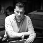 Ein Mann spielt Poker an einem Tisch mit grünen Filz und Chips. Er hält Karten in der Hand und konzentriert sich auf das Spiel.