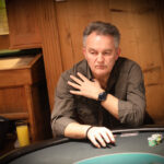 Ein bunter Pokertisch mit Spielkarten, Chips und Getränken, umgeben von verschiedenen Personen, die konzentriert und gespannt spielen.