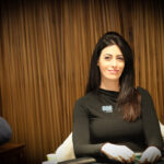 Ein Mann und eine Frau sitzen an einem Pokertisch in einem eleganten Casino. Der Mann hält seine Karten und schaut konzentriert auf den Tisch, während die Frau mit gespanntem Blick auf ihre Karten