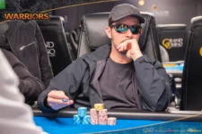 Ein Mann und eine Frau sitzen am Pokertisch und betrachten konzentriert ihre Karten. Der Mann hat eine schwarze Kappe auf und die Frau trägt eine Brille. Im Hintergrund sind Pokerchips und Spiel