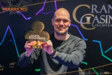Ein professioneller Pokerspieler mit Sonnenbrille und Kappe sitzt an einem grünen Pokertisch, umgeben von Karten und Pokerchips.