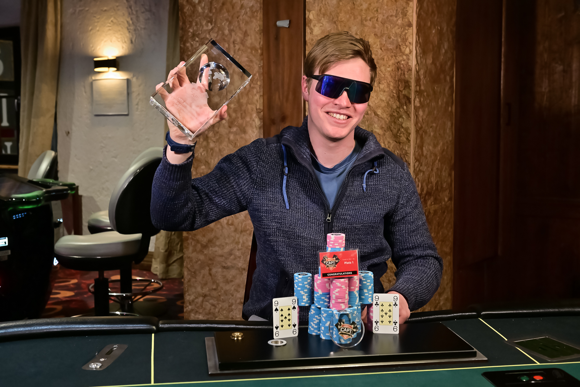 Ein Spieler sitzt an einem Pokertisch während eines Turniers im Casino Seefeld. Er hält Karten in der Hand und schaut konzentriert auf den Tisch. Im Hintergrund sind andere Spieler und Dealer zu sehen