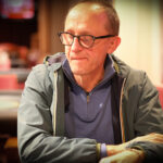Ein Mann sitzt an einem Pokertisch, hält Karten in der Hand und schaut konzentriert auf seine Gegner.