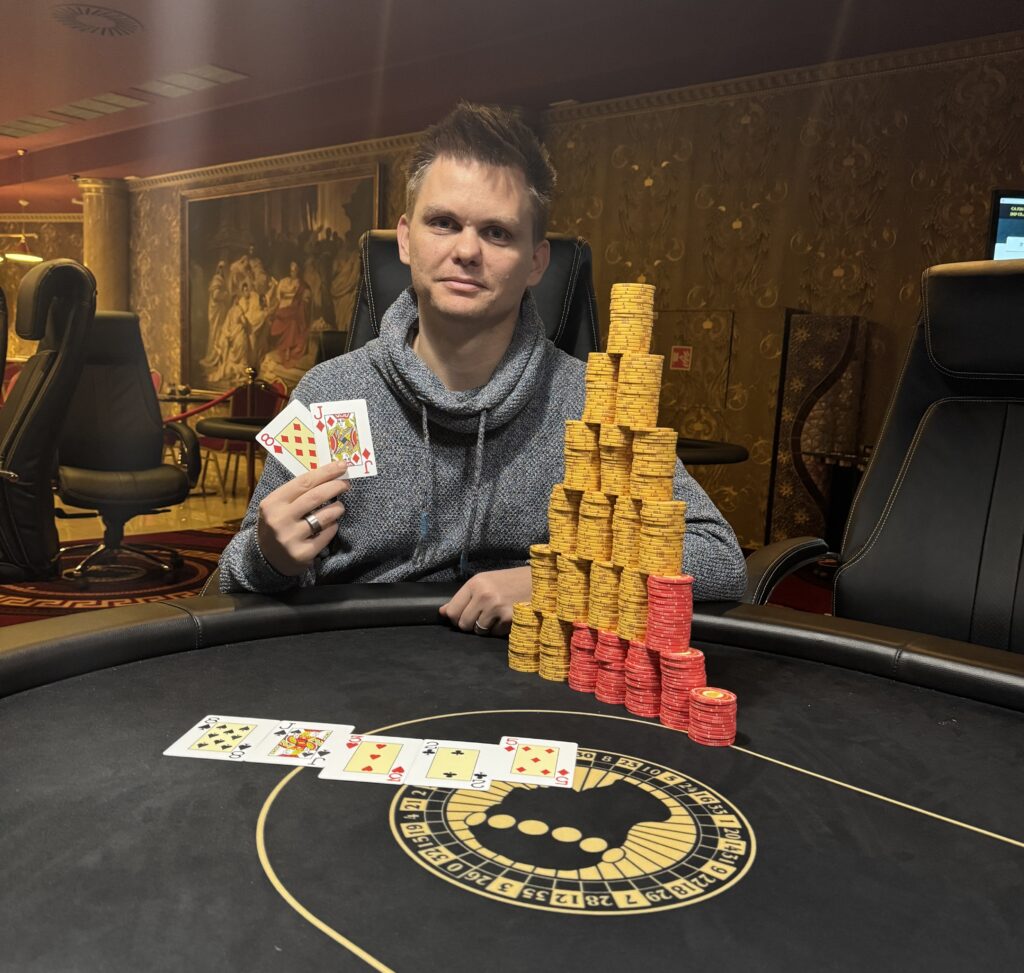 Ein Mann und eine Frau sitzen an einem Pokertisch und halten ihre Karten in der Hand. Der Mann hat einen konzentrierten Blick, während die Frau lächelt. Im Hintergrund sind Pokerchips und Geträn
