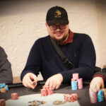 Ein junger Mann namens Maximilian Steinmüller sitzt lächelnd an einem Pokertisch und hält Karten in der Hand.