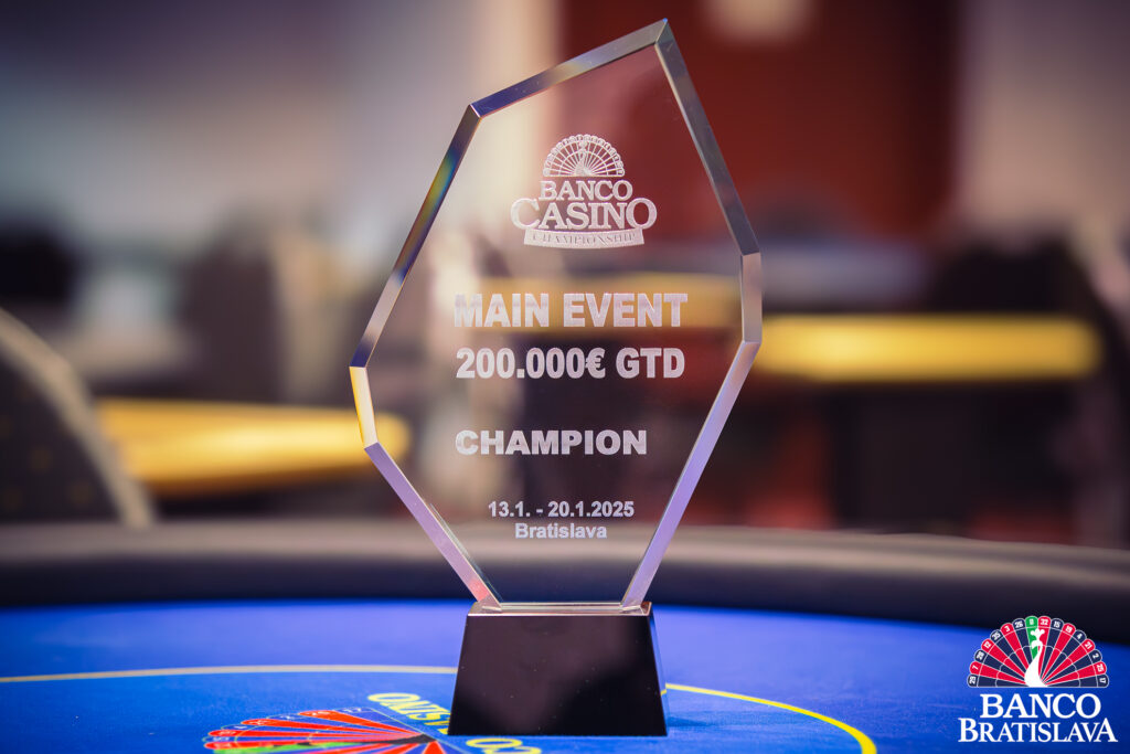 Ein glänzender Pokal auf einem Holztisch, umgeben von Spielkarten und Pokerchips. Der Pokal hat eine goldene Farbe und ist mit Details verziert. Es handelt sich um den Banco Casino Championship