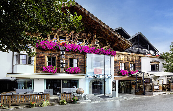 Ein eleganter Pokertisch mit grünem Filz, umgeben von Stühlen und Spielern, die Karten halten und Chips stapeln, in einem stilvollen Casino in Seefeld.