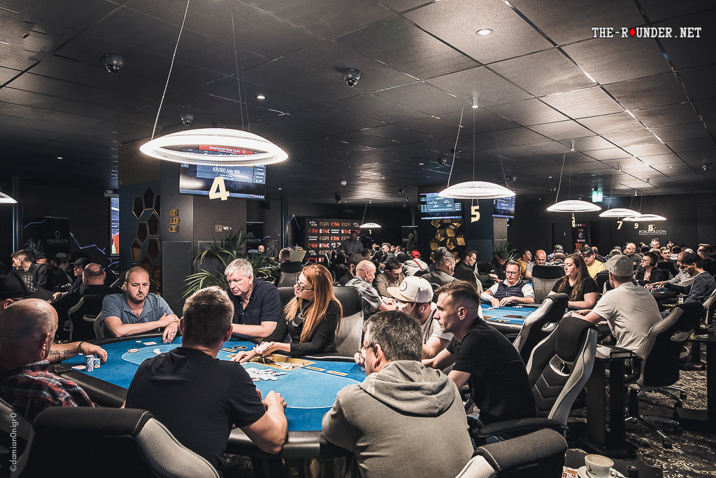 Ein stilvoller Pokerraum mit einem großen Tisch, umgeben von luxuriösen Stühlen und einer eleganten Beleuchtung. In der Mitte des Tisches liegen Spielkarten und Pokerchips. Im
