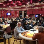 Ein Mann und eine Frau sitzen an einem Pokertisch und spielen Texas Hold'em. Der Mann hat gerade eine Hand gewonnen und streicht seine Chips ein, während die Frau enttäuscht aussieht. Sie tragen elegante