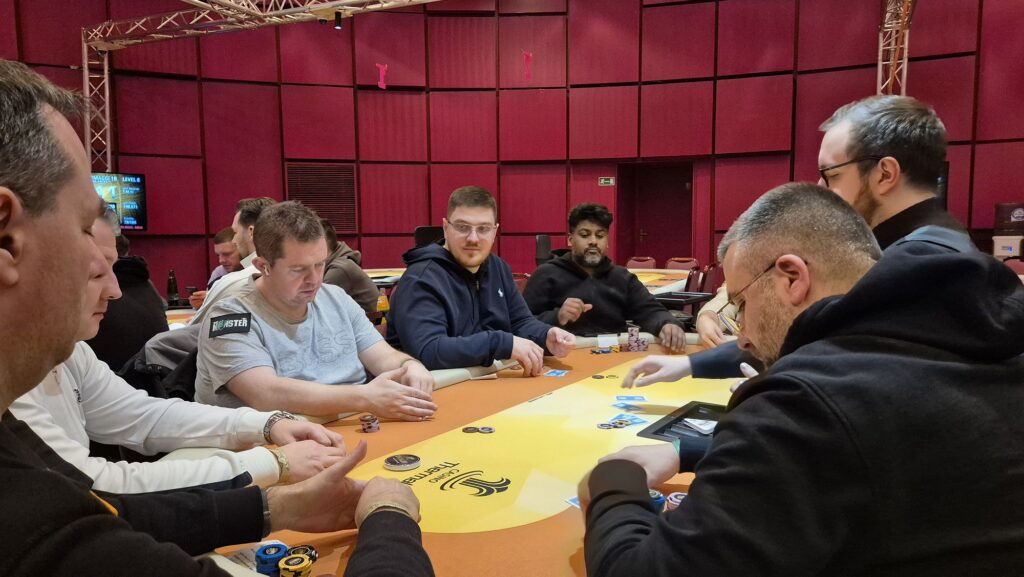 Ein stilllebenartiges Foto einer Pokerrunde mit verschiedenen Spielkarten, Pokerchips und Getränken auf einem Tisch. Es herrscht eine gespannte Atmosphäre, da die Spieler ihre Karten betrachten