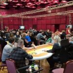 Ein Mann sitzt an einem Pokertisch und hält zwei Könige (König-König) in der Hand. Er hat eine ernste Miene und starrt konzentriert auf seine Karten. Andere
