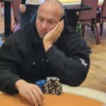 Ein professioneller Pokertisch mit grünem Filz und Chips, Karten und Getränken darauf. Zwei Personen sind dabei, eine Partie Poker zu spielen.
