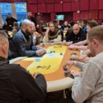 Ein Mann spielt Poker an einem Tisch in einem Casino, umgeben von anderen Spielern und Chips.