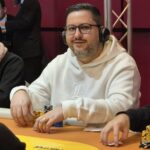 Ein Poker-Tisch mit grüner Filzdecke, umgeben von Spielkarten, Pokerchips und Getränken. Mehrere Personen sitzen um den Tisch und spielen eine Runde Poker.