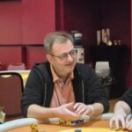 Ein Mann mit einer Pokerkarte in der Hand, der auf einen Tisch schaut.