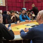 Ein Mann in einem schwarzen Anzug sitzt an einem Pokertisch und hält zwei Könige (König-König) in der Hand. Er schaut konzentriert auf seine Karten, während Chips vor ihm