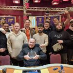 Ein Mann und eine Frau sitzen an einem Pokertisch und spielen eine Partie Poker. Der Mann hat gerade eine Hand gespielt und schaut gespannt auf die Karten in der Mitte des Tisches, während die Frau nach