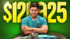 Ein Mann sitzt an einem Pokertisch und filmt sich selbst mit einer Kamera. Er trägt ein dunkles Hemd und eine Brille. Hinter ihm sind Chips und Spielkarten zu sehen.