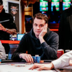 Ein Mann sitzt an einem Pokertisch und betrachtet seine Karten mit ernstem Gesichtsausdruck.
