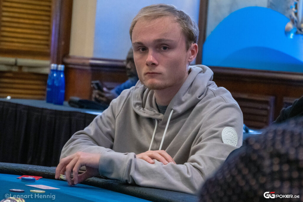 Ein Mann sitzt konzentriert am Pokertisch und überprüft seine Karten während ein Sturm draußen durch die Fenster zu sehen ist.