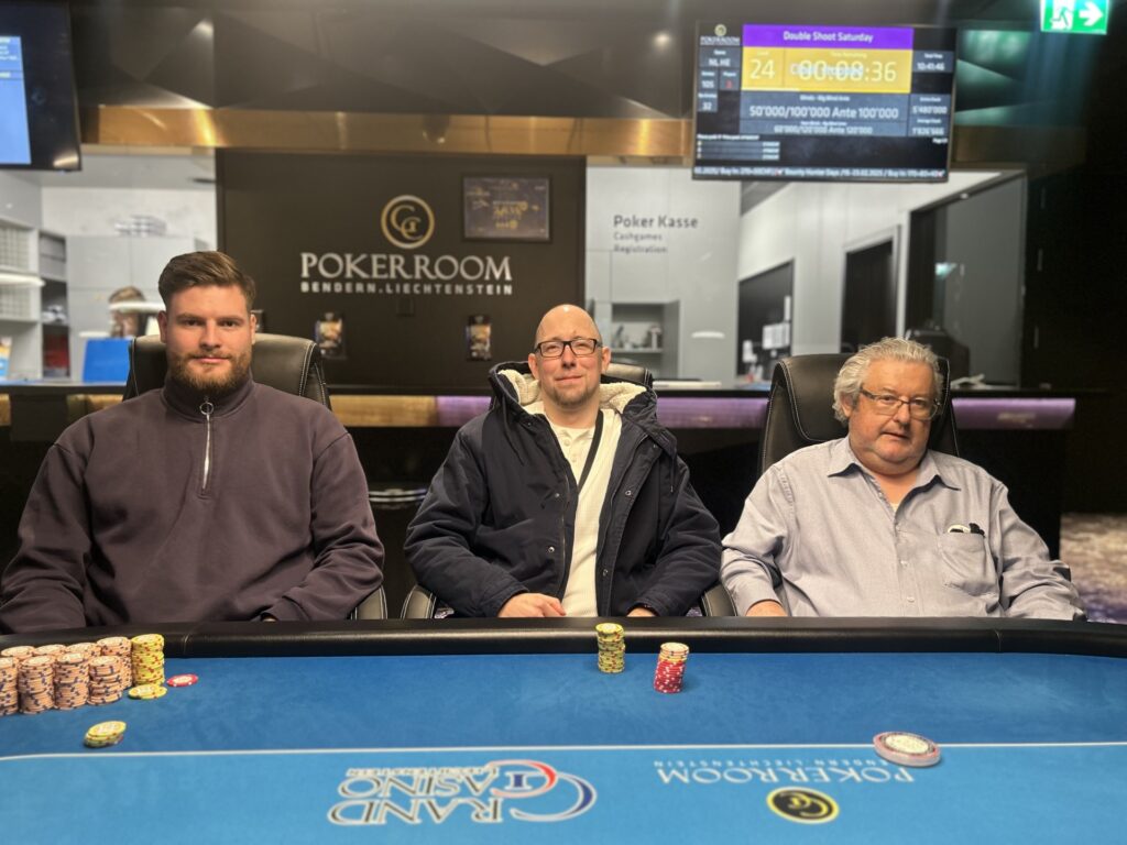 Ein glücklicher Pokerspieler mit einem breiten Lächeln hält zwei Spielkarten in der Hand und zeigt sie der Kamera. Im Hintergrund sind konfettiartige Effekte zu sehen.