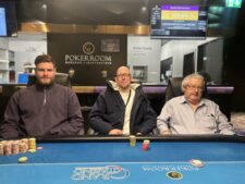 Ein glücklicher Pokerspieler mit einem breiten Lächeln hält zwei Spielkarten in der Hand und zeigt sie der Kamera. Im Hintergrund sind konfettiartige Effekte zu sehen.
