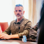 Ein Mann namens Zisis Lianas, der professionell Poker spielt, sitzt an einem Pokertisch in einem Casino und konzentriert sich auf sein Blatt.