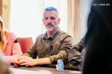 Ein Mann namens Zisis Lianas, der professionell Poker spielt, sitzt an einem Pokertisch in einem Casino und konzentriert sich auf sein Blatt.