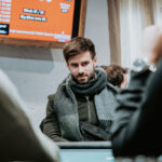 Ein Mann und eine Frau sitzen an einem Pokertisch und spielen Texas Hold'em. Der Mann hat eine Pokerhand aufgedeckt und schaut sie konzentriert an, während die Frau ihre Handkarten betrachtet. Die
