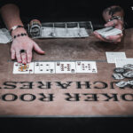 Ein professioneller Pokertisch mit grünem Filz, umgeben von Spielern, die Karten halten und Pokerchips stapeln. Es herrscht eine gespannte Atmosphäre während des Spiels.