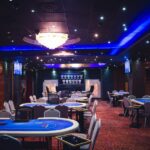 Ein Mann und eine Frau sitzen an einem Pokertisch und halten jeweils Karten in der Hand. Sie scheinen konzentriert und ernsthaft in das Spiel vertieft zu sein. Im Hintergrund sind Pokerch