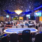 Ein buntes und lebhaftes Bild eines Pokertisches mit Spielkarten, Jetons und Getränken, umgeben von Menschen, die konzentriert und gespannt sind.
