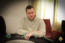 Ein Mann und eine Frau sitzen an einem Pokertisch und spielen Texas Hold'em. Der Mann hält Karten in der Hand, während die Frau mit ernstem Gesichtsausdruck auf ihre eigenen Karten schaut. Im H