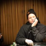 Ein Mann und eine Frau sitzen in einem eleganten Casino und spielen Poker. Der Mann trägt einen Anzug und eine Krawatte, die Frau hat ein elegantes Abendkleid an. Sie haben ernste Gesichter und halten