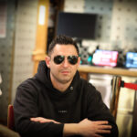 Ein Mann und eine Frau sitzen an einem Pokertisch und betrachten konzentriert ihre Karten. Eine grüne Pokertischdecke ist zu sehen, sowie Pokerchips und Spielkarten. Die Frau trägt eine