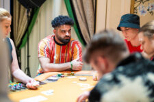 Ein Mann sitzt an einem Pokertisch, umgeben von Chips und Karten. Er trägt eine Sonnenbrille und hat eine ernste Miene.