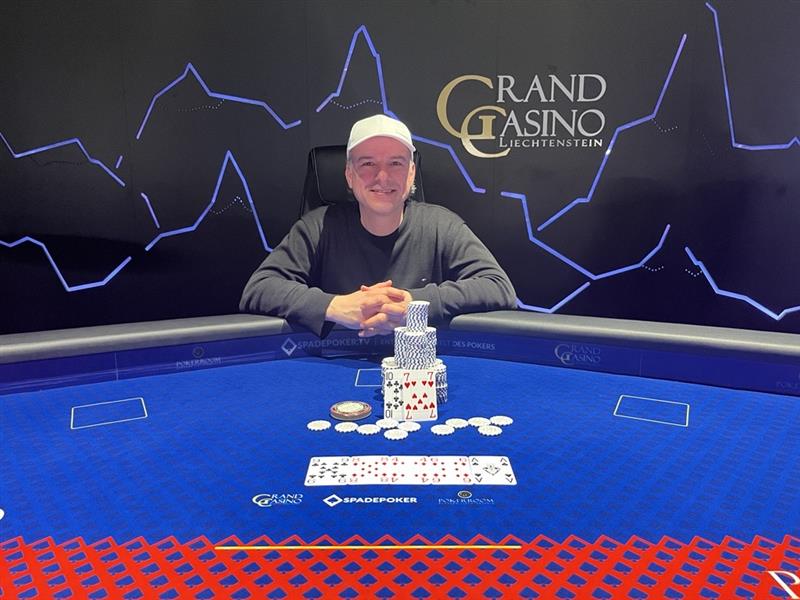Ein Mann sitzt an einem Pokertisch mit einem großen Stapel Chips vor sich. Er betrachtet konzentriert seine Karten.