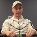 Ein Mann und eine Frau sitzen an einem Pokertisch und spielen eine Partie Poker. Der Mann hat einen ernsten Gesichtsausdruck und hält seine Karten in der Hand, während die Frau lächelt und Chips stap