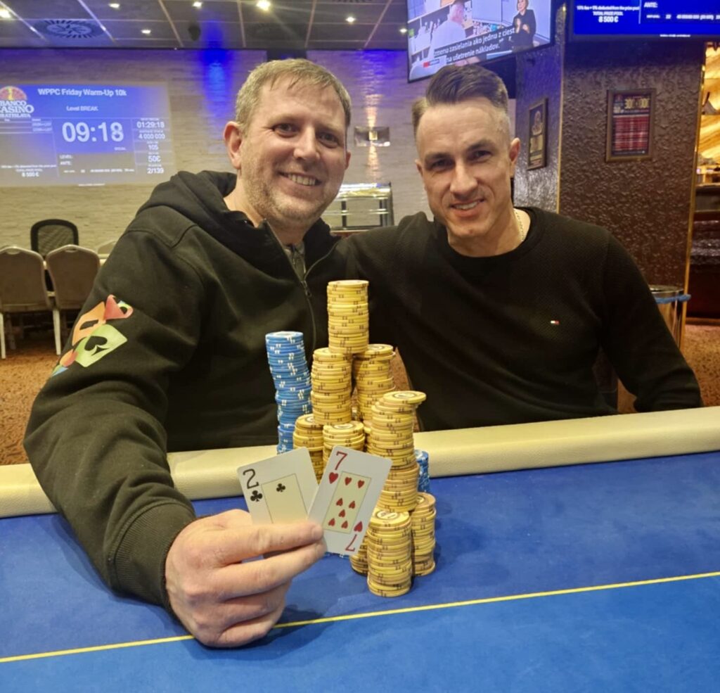 Ein Mann und eine Frau sitzen am Pokertisch und spielen Texas Hold'em. Sie halten Karten in der Hand und haben Pokerchips vor sich liegen. Der Mann hat eine Kappe auf und die Frau trägt eine Brille.