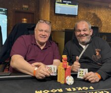Ein Mann sitzt an einem Pokertisch und hält seine Spielkarten in der Hand, während er konzentriert auf die Mitte des Tisches schaut. Um ihn herum sind Pokerchips und eine Mischmaschine
