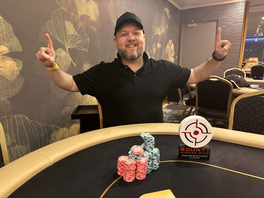 Ein Mann und eine Frau sitzen lächelnd an einem Pokertisch und spielen Karten. Der Mann hält Karten in der Hand und die Frau schaut konzentriert auf ihre eigenen Karten. Im Hintergrund sind