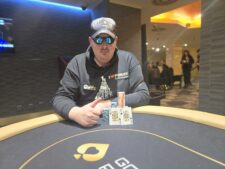 Ein Foto von einem Pokertisch während eines Turniers mit Stapeln von Pokerchips und Spielkarten darauf. Die Spieler sind konzentriert und entschlossen, während sie ihre Hände spielen. Ein Dealer sitzt am Tisch